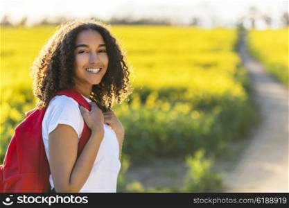 Outdoor portrait in golden evening sunshine of beautiful happy mixed race African American girl teenager female young woman smiling laughing with perfect teeth hiking with red recksack in yellow field