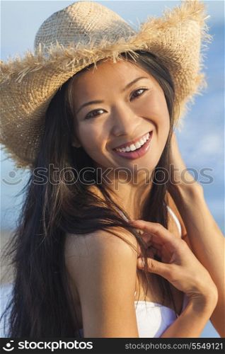 Outdoor portrait of a beautiful Chinese Asian young woman or girl wearing a white bikini and straw cowboy hat at a beach
