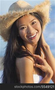 Outdoor portrait of a beautiful Chinese Asian young woman or girl wearing a white bikini and straw cowboy hat at a beach