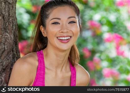 Outdoor portrait of a beautiful happy fit healthy young Chinese Asian young woman or girl laughing with perfect teeth wearing pink running vest with natural flower background