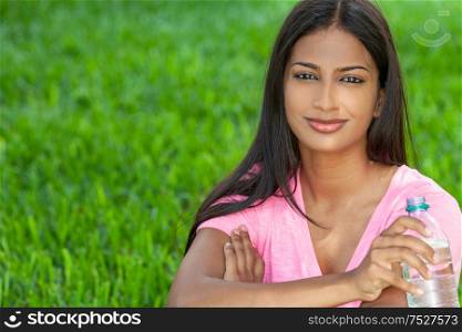 Outdoor portrait of a beautiful happy Indian Asian young woman or girl outside in summer sunshine drinking from a bottle of water