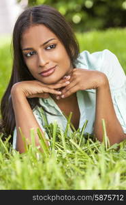 Outdoor portrait of a beautiful Indian Asian young woman or girl outside in summer sunshine laying down resting on her hands