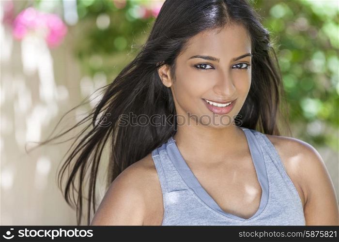 Outdoor portrait of a beautiful Indian Asian young woman or girl outside in summer sunshine with perfect teeth and long hair exercising wearing health and fitness clothing