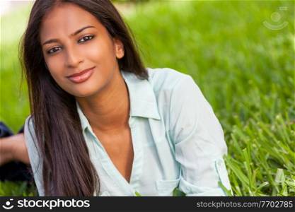 Outdoor portrait of a beautiful Indian Asian young woman or girl outside in summer sunshine happy smiling laying down on grass
