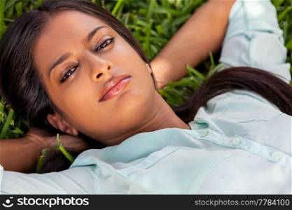 Outdoor portrait of a beautiful Indian Asian young woman or girl outside in summer sunshine laying down on grass
