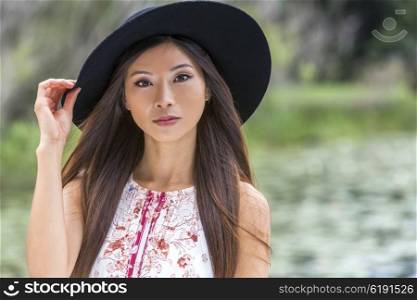 Outdoor portrait of a beautiful thoughtful young Chinese Asian young woman or girl wearing a summer dress and a black hat