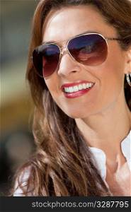 Outdoor portrait of a beautiful young brunette woman in her thirties wearing aviator sunglasses with a perfect toothy smile