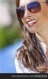Outdoor portrait of a beautiful young brunette woman in her thirties wearing aviator style sunglasses