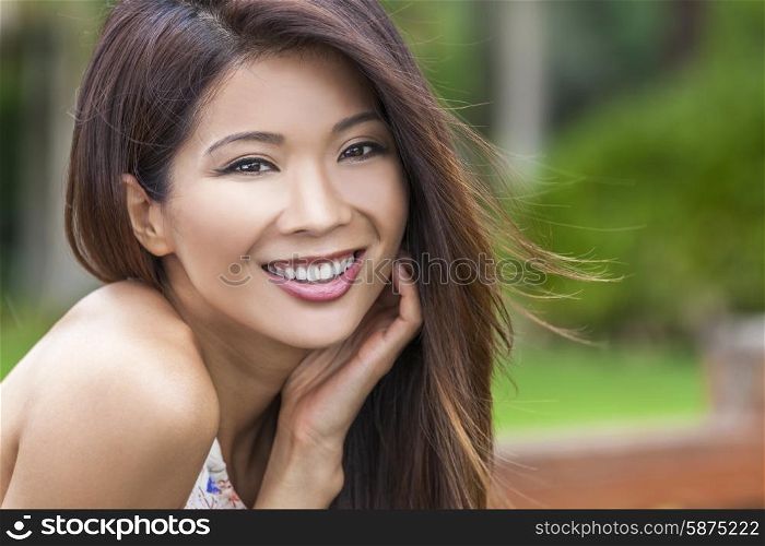 Outdoor portrait of a beautiful young Chinese Asian young woman or girl with perfect teeth, smiling and resting in her hand