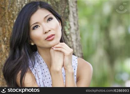 Outdoor portrait of a beautiful young Chinese Asian young woman or girl with natural green background