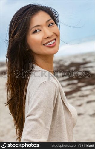 Outdoor portrait of a beautiful young Chinese Asian young woman or girl walking on a beach smiling with perfect teeth