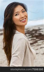 Outdoor portrait of a beautiful young Chinese Asian young woman or girl walking on a beach smiling with perfect teeth