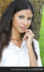 Outdoor portrait of a beautiful young Latina Hispanic girl or young woman leaning against a tree