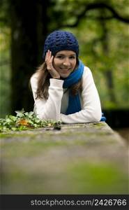 Outdoor portrait of a beautiful young woman lying on a stonewall
