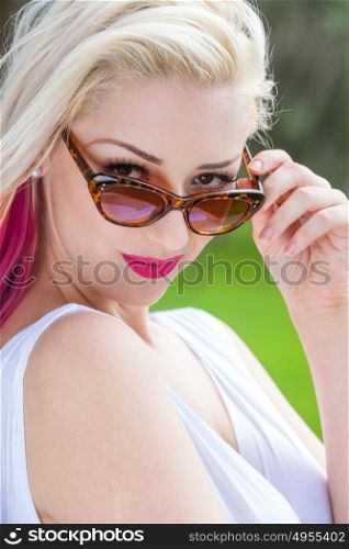 Outdoor portrait of a beautiful young woman or girl with blond and pink hair wearing sunglasses outside