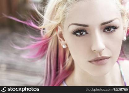 Outdoor portrait of a beautiful young woman or girl with brown eyes, blond and magenta pink hair