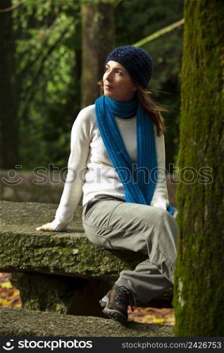 Outdoor portrait of a beautiful young woman sitting on a stone wall