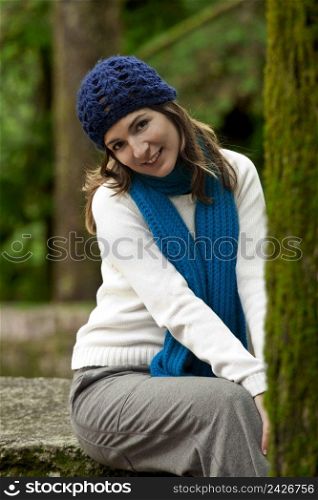 Outdoor portrait of a beautiful young woman sitting on a stone wall