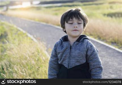 Outdoor portrait of a cute smiling boy with a closed eyes, A happy kid breathes the fresh air from nature. Relaxed boy breathing fresh air in a farm field.