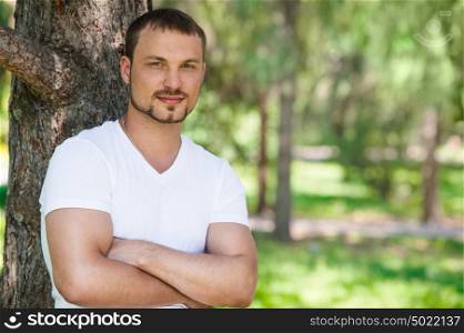 Outdoor portrait of a good looking young man leaning on tree at summer park
