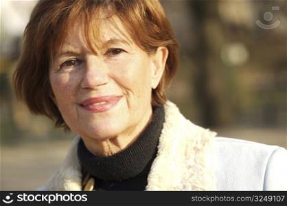 Outdoor portrait of a smiling senior woman in late afternoon sunlight.