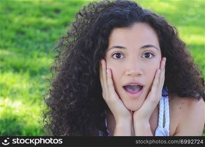 Outdoor portrait of a young beautiful latin woman with surprised facial expression on a summer park background.