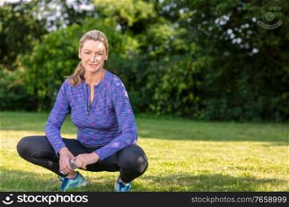 Outdoor portrait of an attractive middle aged blonde woman smiling drinking water relaxing after exercising, running or fitness lifestyle