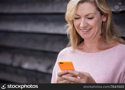 Outdoor portrait of an attractive middle aged blonde woman smiling using mobile cell phone for text messaging or social media