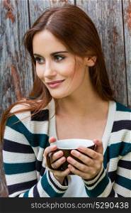 Outdoor portrait of beautiful girl or young woman with red hair drinking tea or coffee