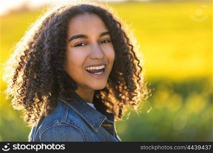 Outdoor portrait of beautiful happy mixed race African American girl teenager female young woman smiling laughing with perfect teeth in field of yellow flowers