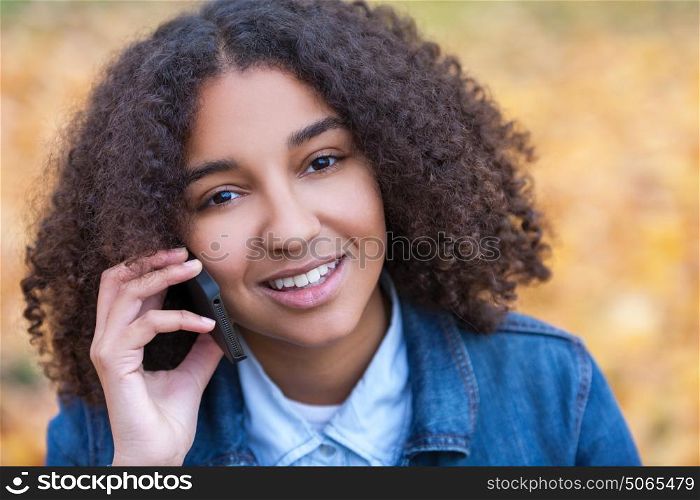 Outdoor portrait of beautiful happy mixed race African American girl teenager female young woman smiling with perfect teeth talking on cell phone