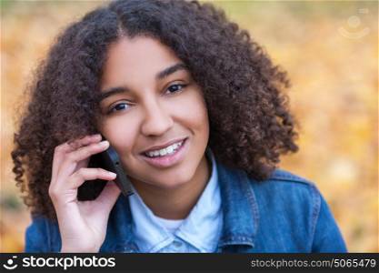 Outdoor portrait of beautiful happy mixed race African American girl teenager female young woman smiling with perfect teeth talking on cell phone