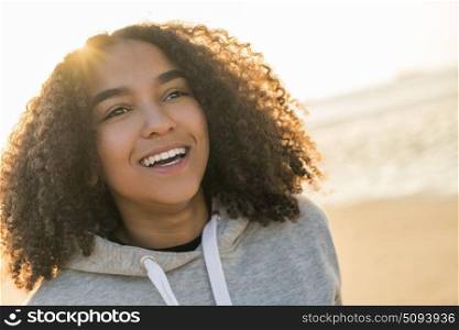 Outdoor portrait of beautiful happy mixed race African American girl teenager female young woman on a beach smiling laughing with perfect teeth in golden sunset evening sunshine