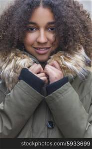 Outdoor portrait of beautiful happy mixed race African American girl teenager female young woman child smiling wrapped up wearing warm fake fur lined coat in winter