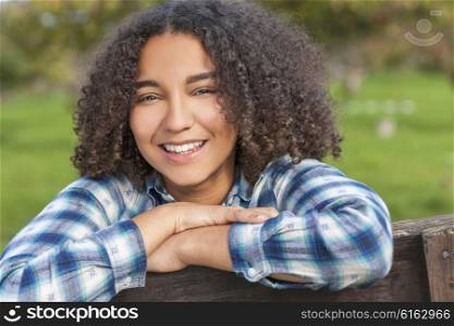 Outdoor portrait of beautiful happy mixed race African American girl teenager female child resting on countryside fence smiling with perfect teeth