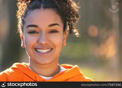 Outdoor portrait of beautiful happy mixed race African American girl teenager female young woman smiling with perfect teeth in golden evening sunshine
