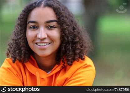 Outdoor portrait of beautiful happy mixed race biracial African American girl teenager female young woman smiling with perfect teeth and wearing an orange hoodie