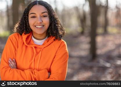 Outdoor portrait of beautiful happy mixed race biracial African American girl teenager female young woman arms folded laughing and smiling with perfect teeth in golden evening sunshine