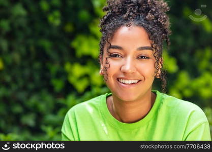 Outdoor portrait of beautiful happy mixed race biracial African American girl teenager female young woman smiling with perfect teeth wearing a green t-shirt