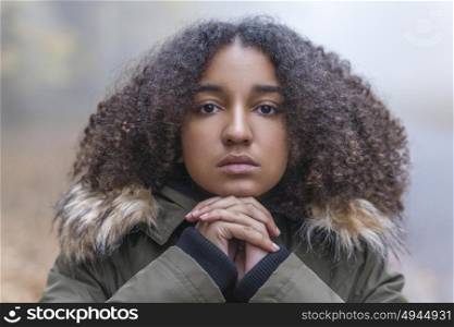 Outdoor portrait of beautiful mixed race African American girl teenager female child resting on her hands outside in a park on foggy day