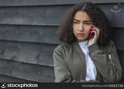 Outdoor portrait of beautiful sad aggressive mixed race African American girl teenager female young woman talking on red cell phone wearing green bomber jacket