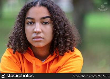 Outdoor portrait of beautiful sad, thoughtful or depressed mixed race biracial African American girl teenager female young woman smiling wearing an orange hoodie