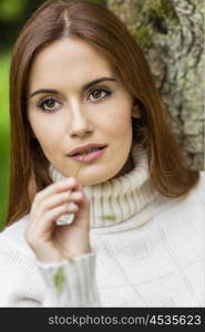 Outdoor portrait of beautiful thoughtful girl or young woman with red hair wearing a jumper and chewing a piece of grass