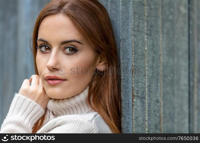 Outdoor portrait of beautiful thoughtful girl or young woman with red hair wearing a white sweater in an urban city environment