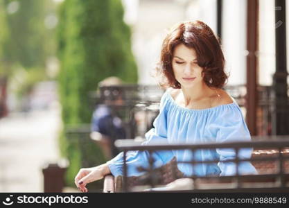 Outdoor portrait of beautiful woman at the table in a street city cafe. Urban romantic portrait of beautiful girl wearing light blue dress and burgundy tights