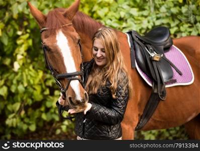 Outdoor portrait of beautiful woman feeding brown horse from hand