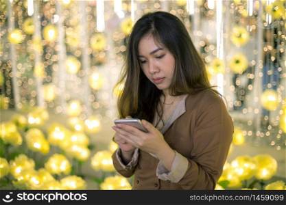 Outdoor portrait of beautiful young asian woman using her mobile phone at night.