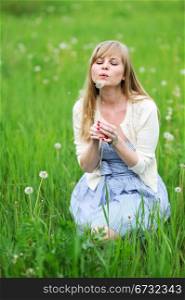 Outdoor portrait of beautiful young blond woman blowing away a dandelion