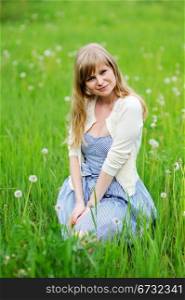 Outdoor portrait of beautiful young blond woman sitting in dandelion field