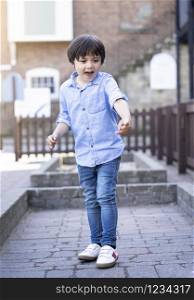 Outdoor portrait of handsome boy standing alone with smiling face, Selective focus happy Child playing outside with blurry building background, Kid relaxing with family on summer holiday.